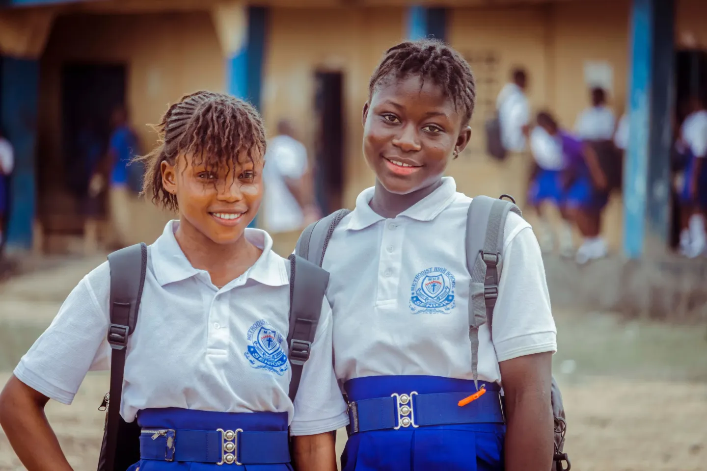 Two adolescent girls stand outside a school in Sierra Leone.