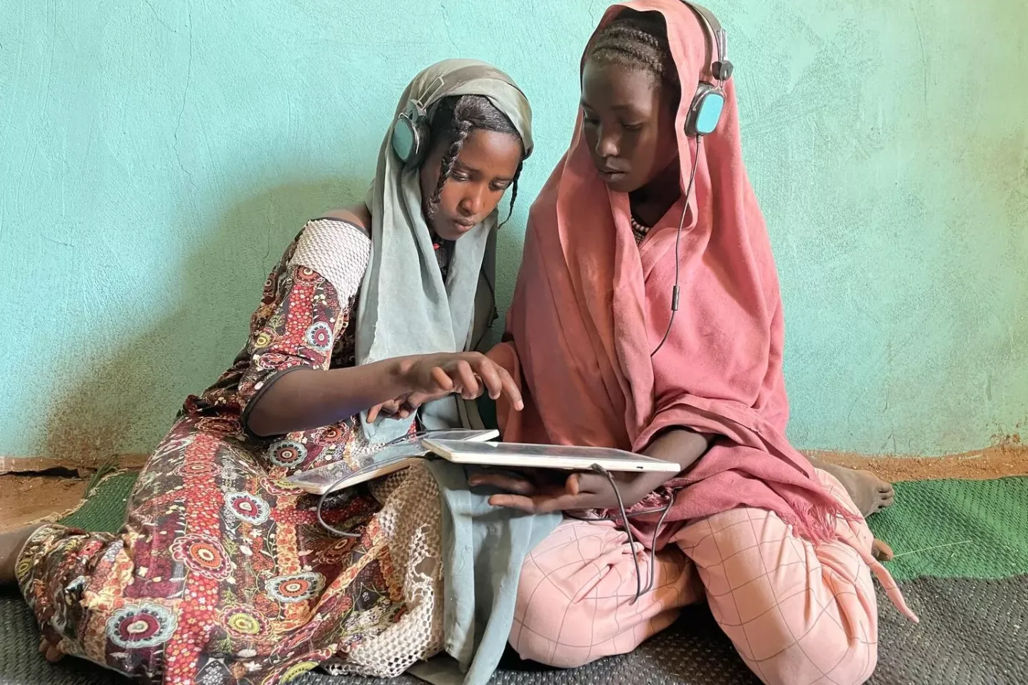 Amal (13, left) and Sarah (13, right) play educational games on their solar-powered tablet in the UNICEF-supported e-learning center in Jabalain, White Nile state, Sudan.