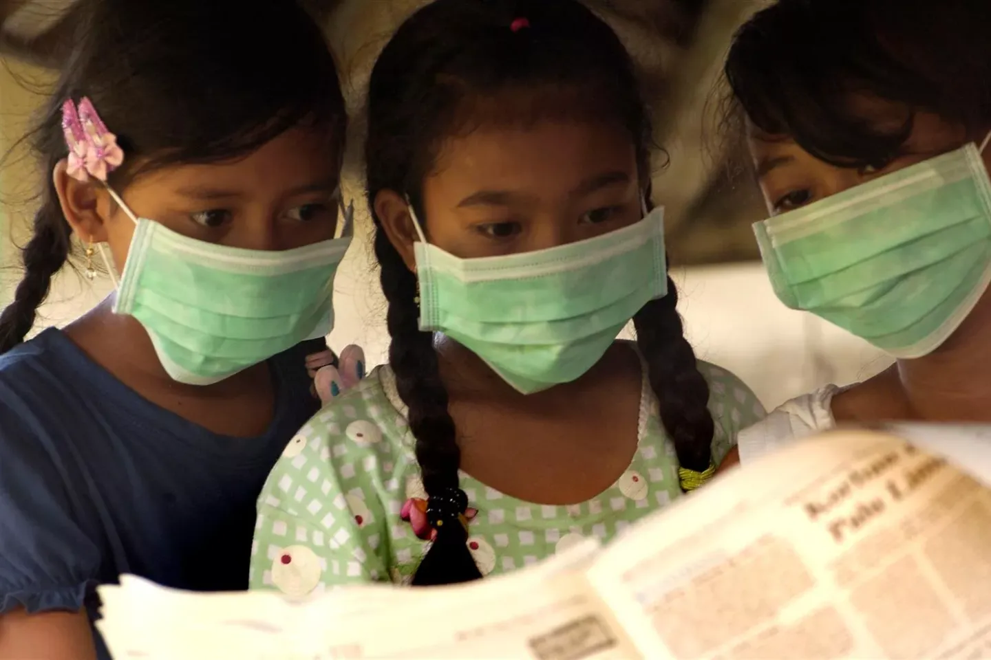 Children read a newspaper while wearing masks during avian flu pandemic simulation at Dangintukadaya village in Jembrana